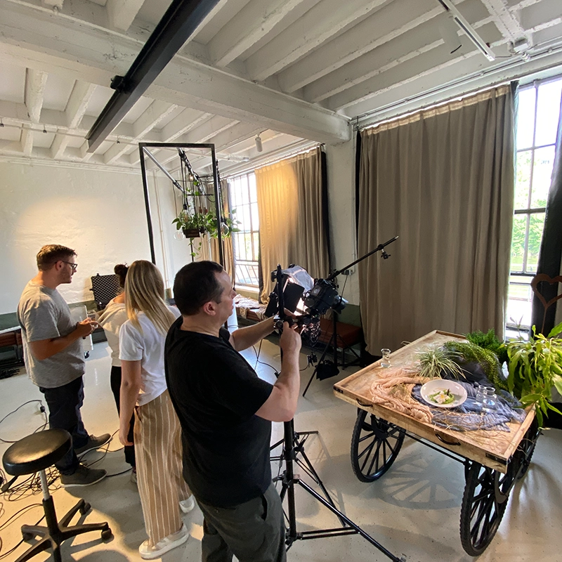 Fotografen-Team bei einem Fotoshooting in einem Studio. Kamera auf ein mit Pflanzen dekoriertes Tablett gerichtet.